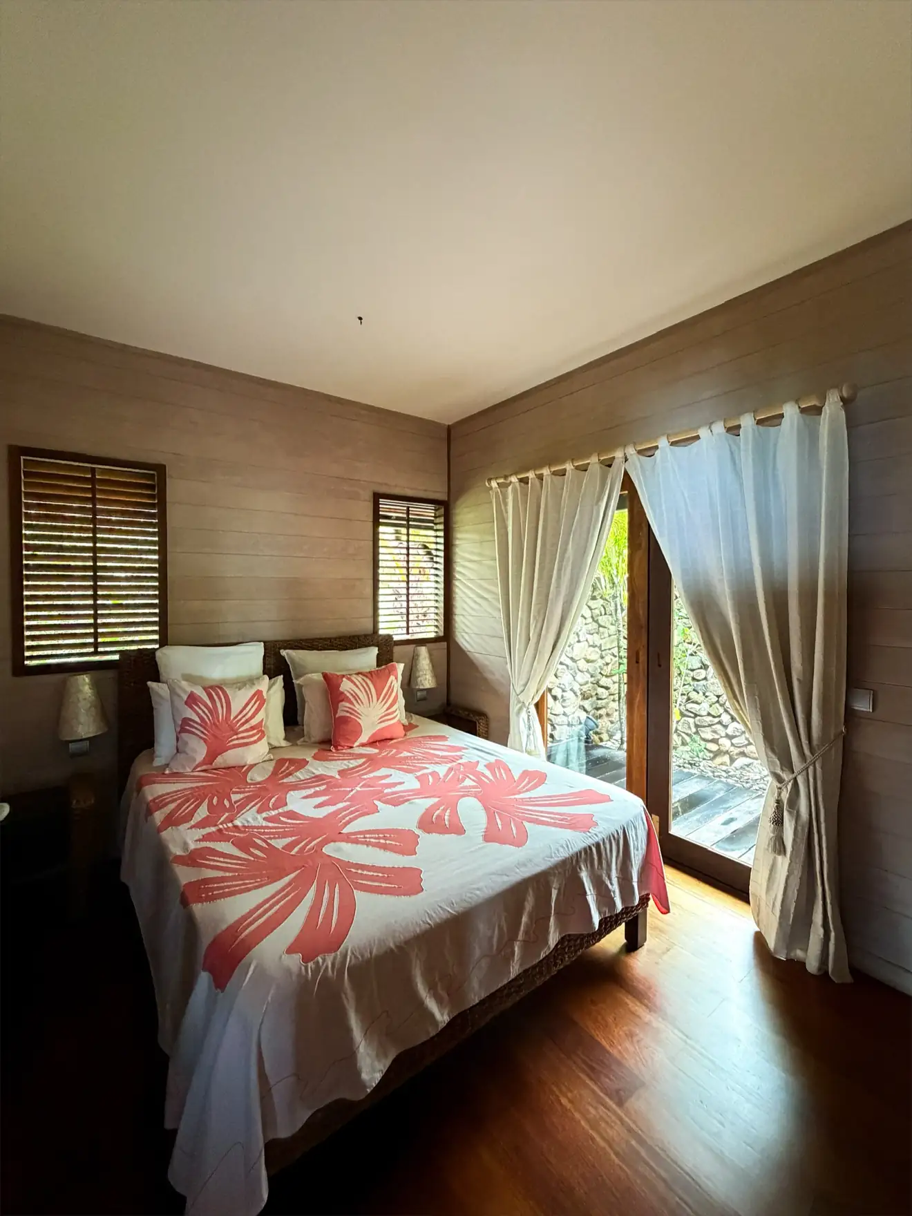 Chambre avec lit queen size, dessus-de-lit blanc et rose, porte-fenêtre sur le jardin